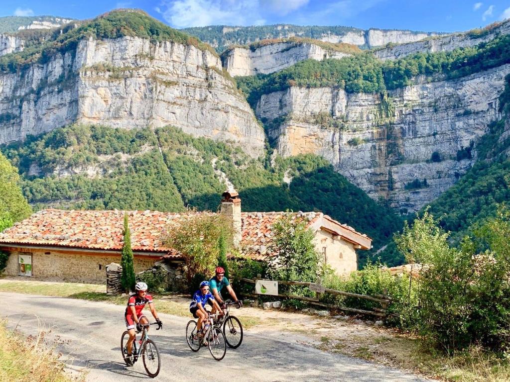 3 Personen fahren Fahrrad auf einer Straße mit Bergen im Hintergrund in der Unterkunft L'Echappée en Vercors in Choranche
