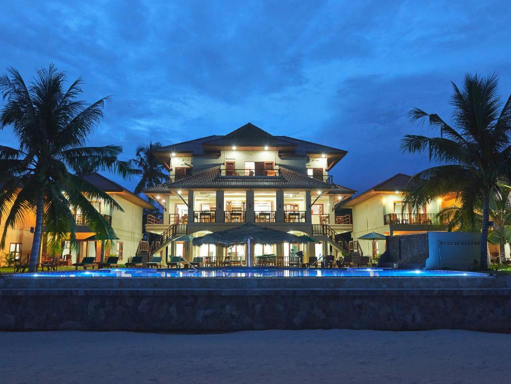 un grand bâtiment avec des palmiers devant lui dans l'établissement Sara Beachfront Boutique Resort, à Pathiu