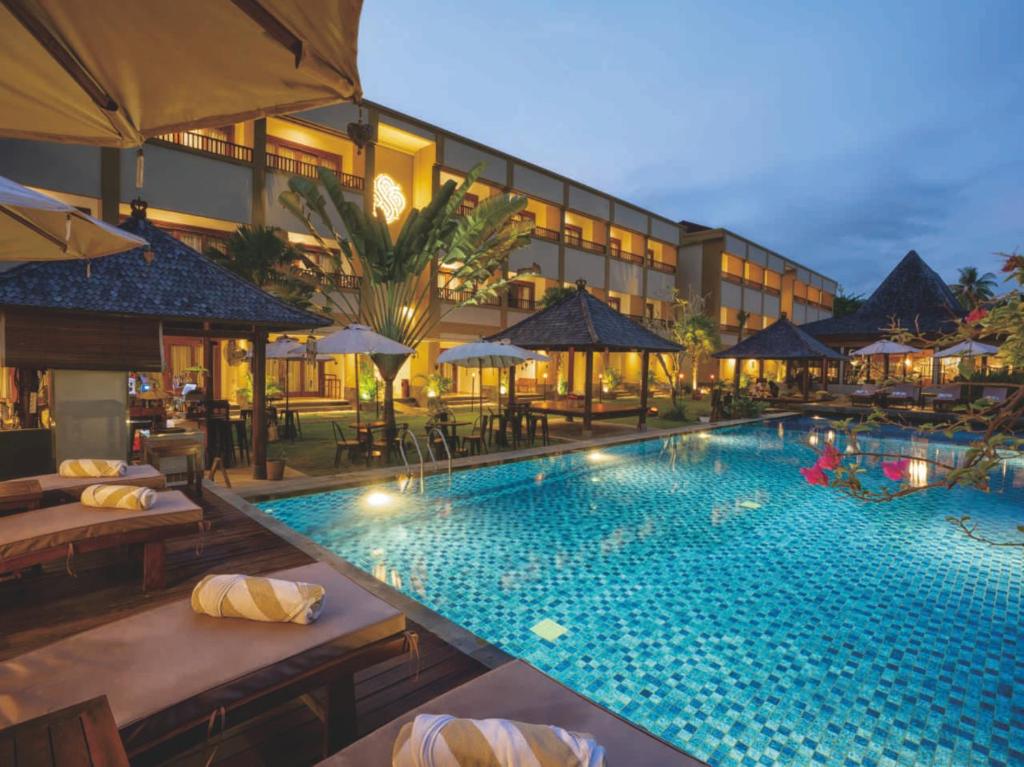 a pool at a hotel with tables and umbrellas at Sima Hotel Kuta Lombok in Kuta Lombok