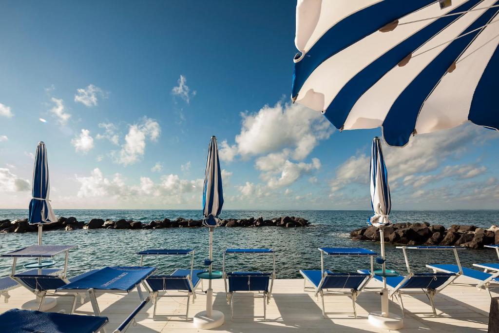 eine Gruppe von Stühlen und Sonnenschirmen am Strand in der Unterkunft Ischia Blu Resort in Ischia