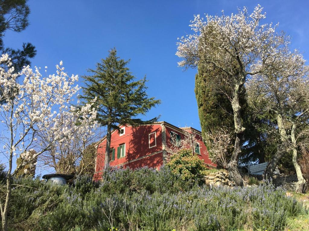 czerwony dom stojący na szczycie wzgórza z drzewami w obiekcie Piccola casa toscana con giardino con vista mozzafiato w mieście Podere Cordicella
