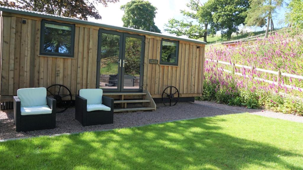 a tiny house with two chairs and a fence at Little Acorn - Luxury shepherd's hut / lodge with private hot tub and garden in Llanfyllin