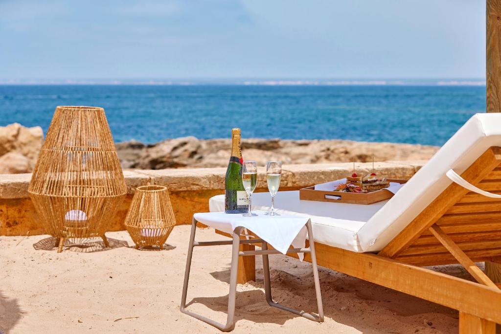 a table with a bottle of champagne and a chair on the beach at Universal Hotel Cabo Blanco - Adults Only in Colonia Sant Jordi