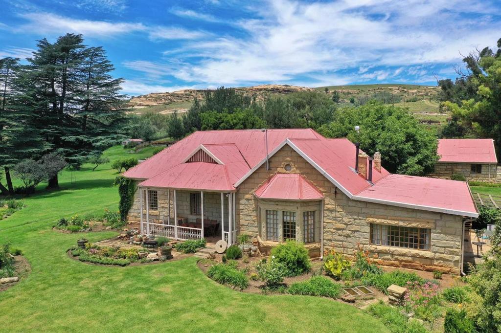 a house with a red roof on a green yard at St Fort Farm Guesthouse in Clarens