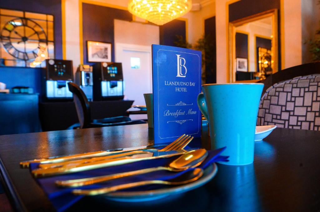 a table with a blue cup and a plate of utensils at Llandudno Bay Hotel in Llandudno