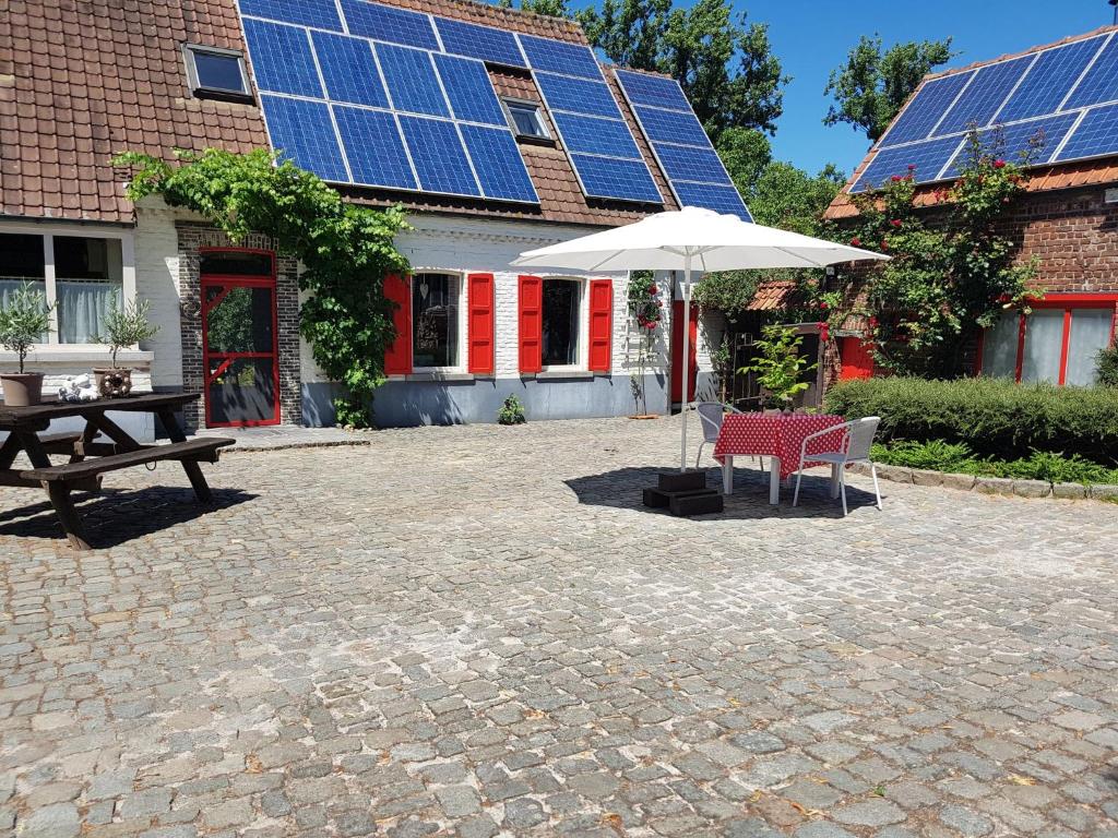 un patio con tavolo e ombrellone e un edificio con pannelli solari di B&B Adem a Horebeke