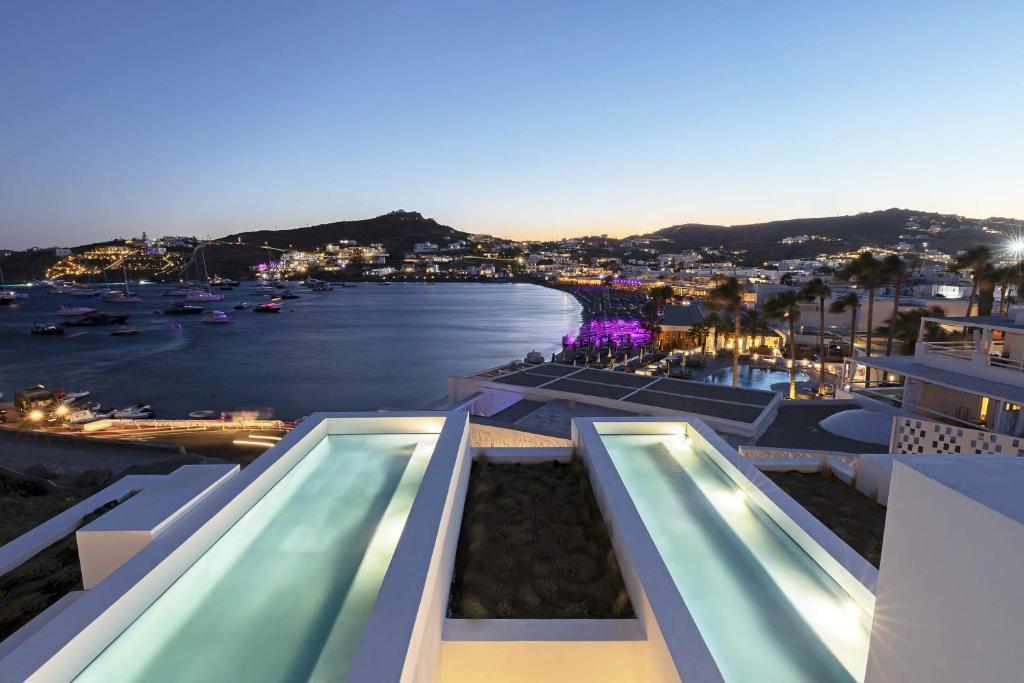 - une vue sur l'eau depuis un bâtiment avec 2 piscines dans l'établissement CUBIC Mykonos Seafront Design Suites, à Ornos