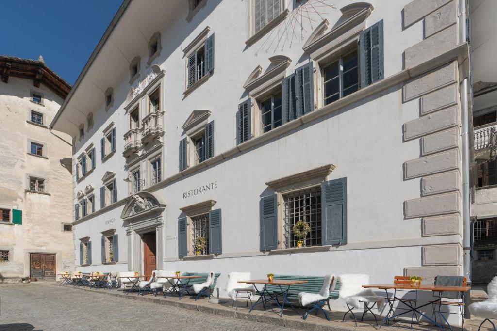 a white building with tables and chairs on a street at Hotel Palazzo Salis in Soglio