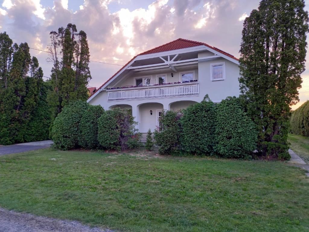 a white house with a balcony and bushes at Hévízi fecskefészek in Hévíz