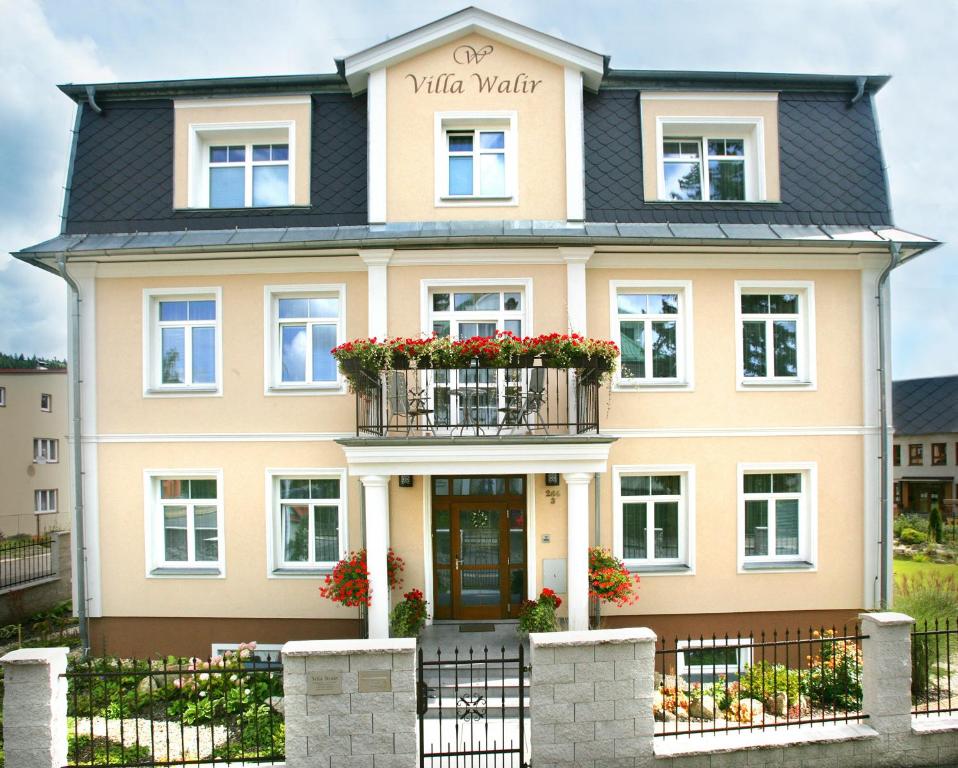 a large yellow house with a balcony with red flowers at Villa Walir - Spa Hotel Garni SUPERIOR in Mariánské Lázně