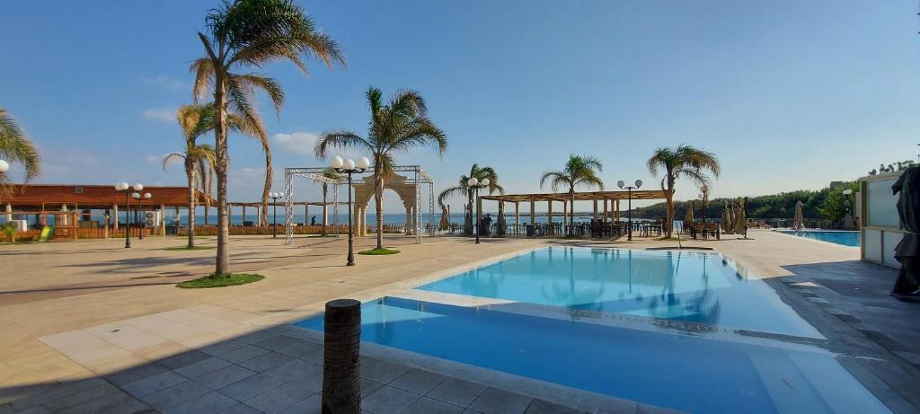 a swimming pool with palm trees and a building at Aquarius Touristic Resort in Al Minyah