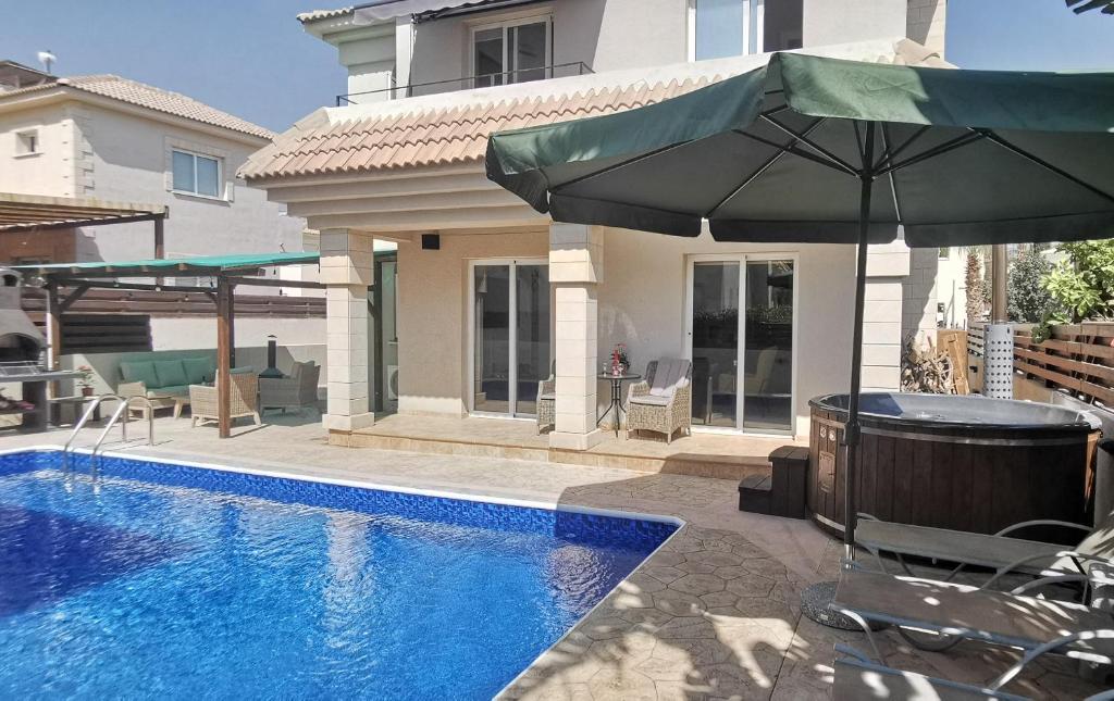 a swimming pool with an umbrella next to a house at GREAT VILLA MARIA in Paralimni