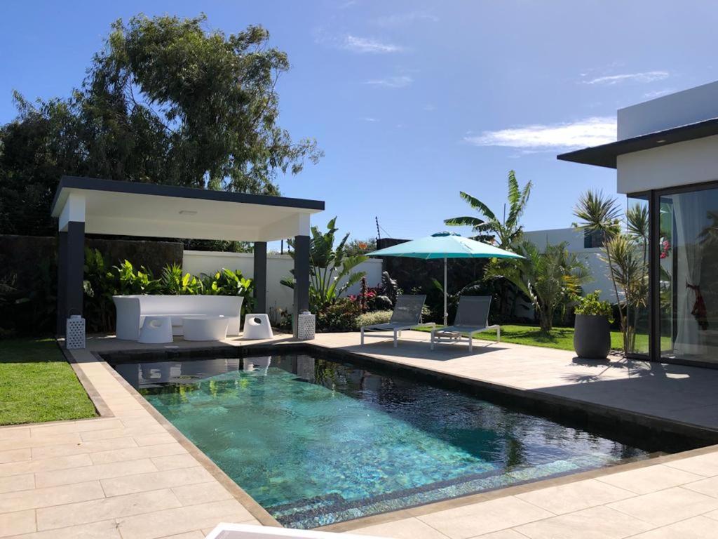 una piscina con sillas y un patio con sombrilla en L'Idéale : Villa neuve et cosy, piscine privative et chauffée, en Cap Malheureux