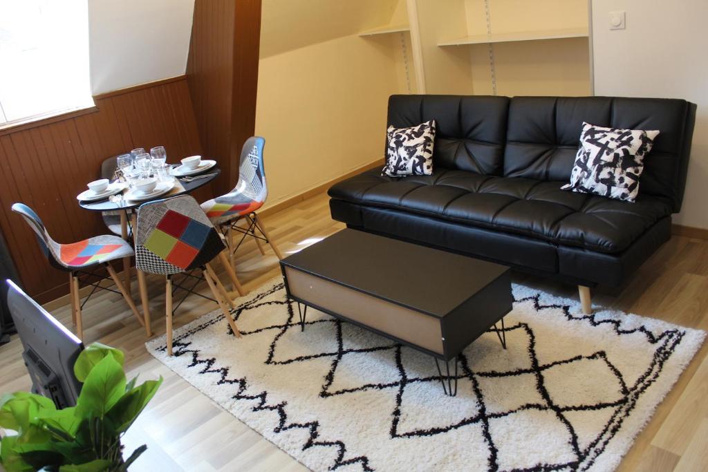 a living room with a black leather couch and a table at LES COTTAGES DU PRYTANEE in La Flèche