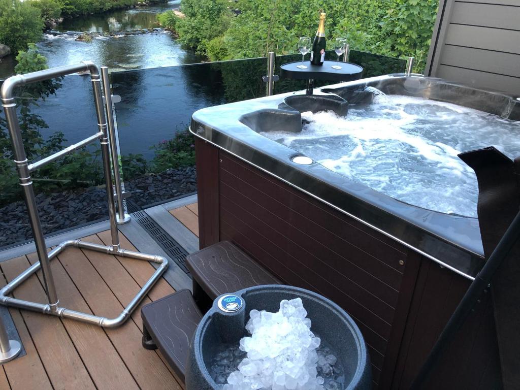 a hot tub on a deck next to a river at Honey lodge in Caeathro