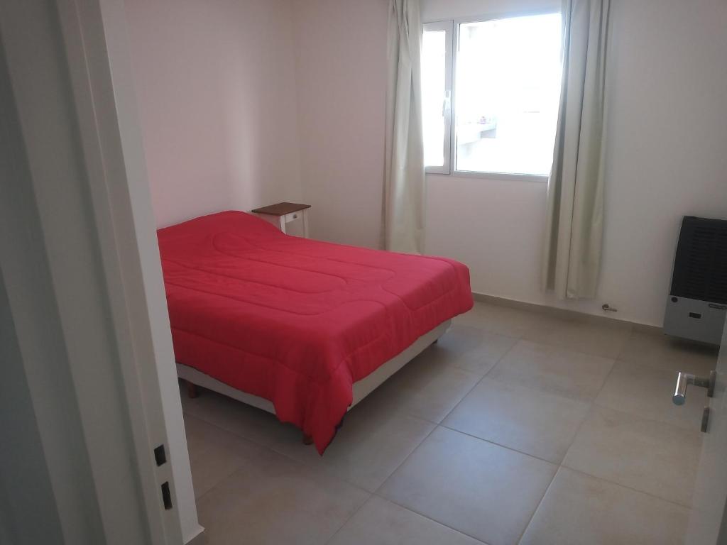 Cama roja en habitación blanca con ventana en El Serrano, en Tandil