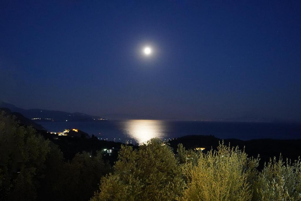 una luna llena elevándose sobre el agua por la noche en Moonlight Suites en Parga