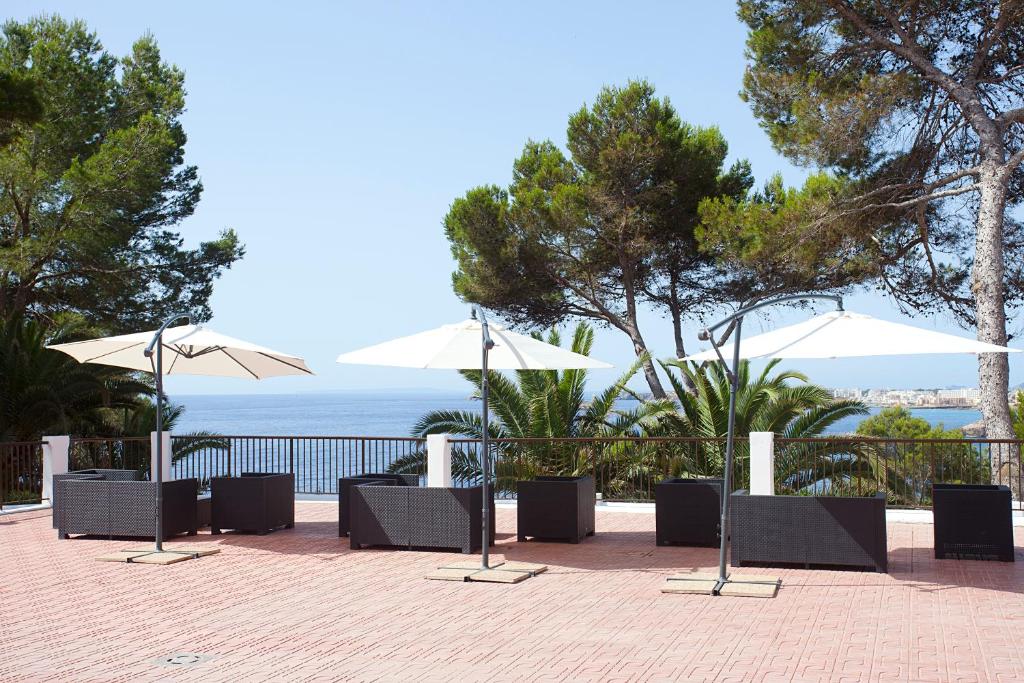 a row of tables and umbrellas on a brick patio at Apartamentos Club Cala Azul in Cala Llenya