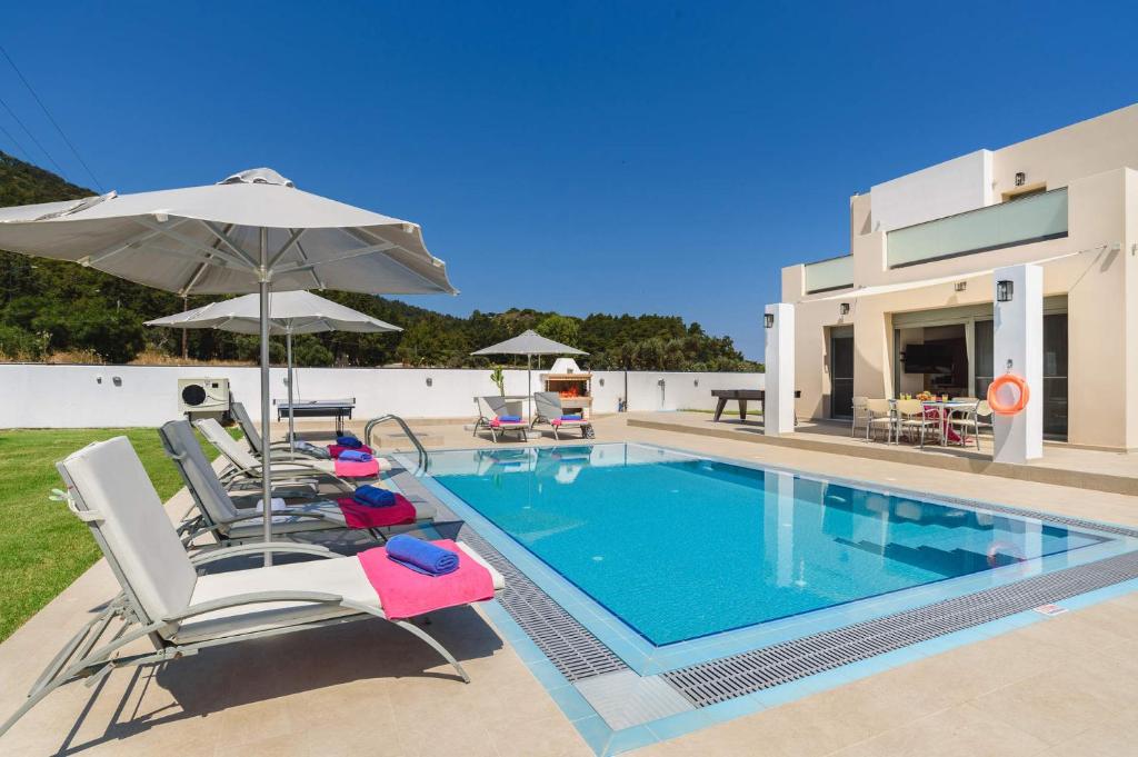 a villa with a swimming pool with chairs and an umbrella at Villa Paleos Hillside by Villa Plus in Ialysos