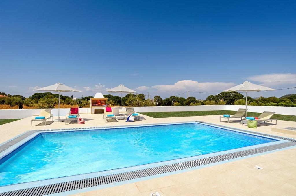 a large swimming pool with chairs and umbrellas at Villa Paleos Aegean by Villa Plus in Ialyssos