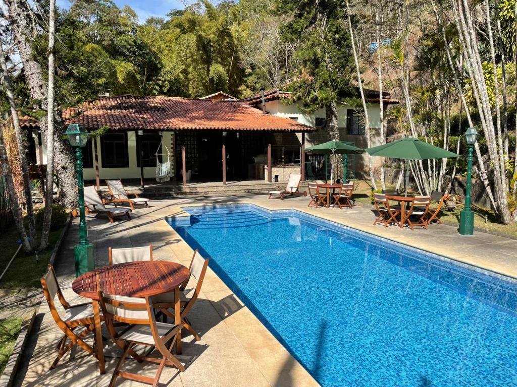 a swimming pool with chairs and tables and a house at Pousada Cozy House in Itaipava