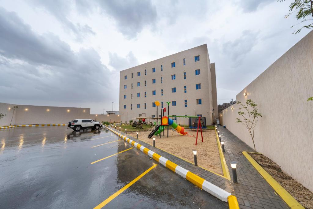 a parking lot with a building and a playground at Ahad Rafidah Garden Millennium Hotel in Khamis Mushayt