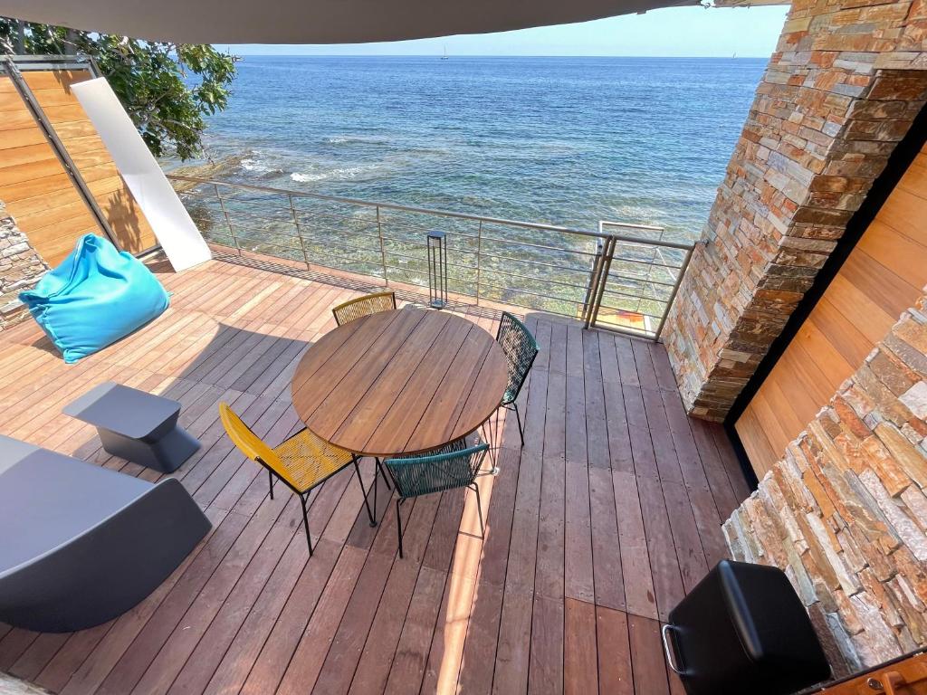 a wooden deck with a table and chairs and the ocean at miomo bord de mer in Santa-Maria-di-Lota