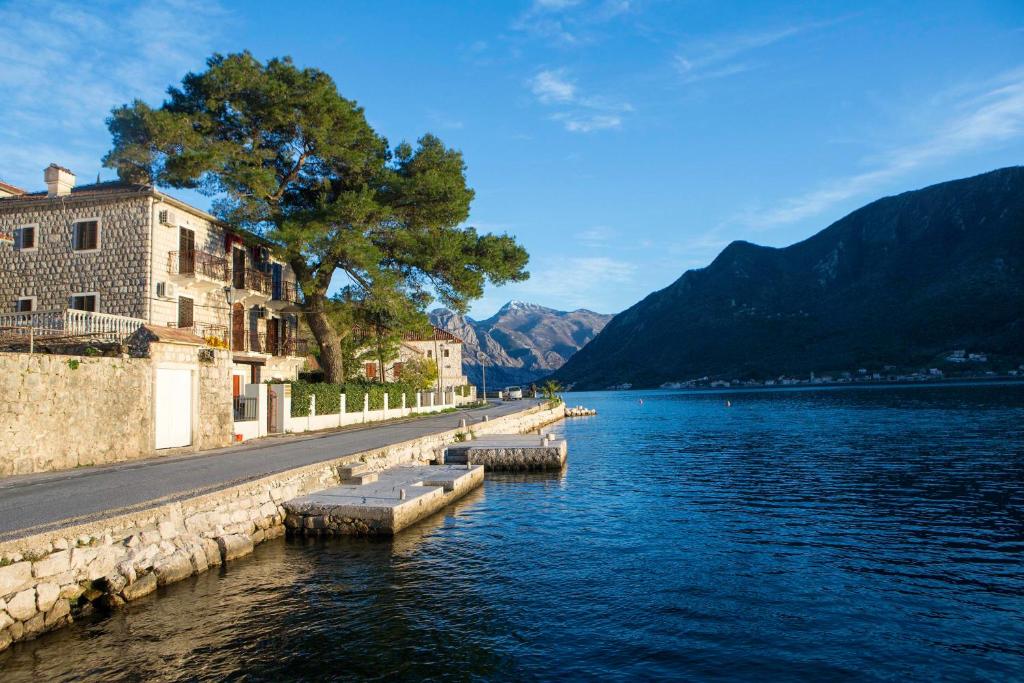 una masa de agua con un edificio y árboles y montañas en Spring Apartment en Perast