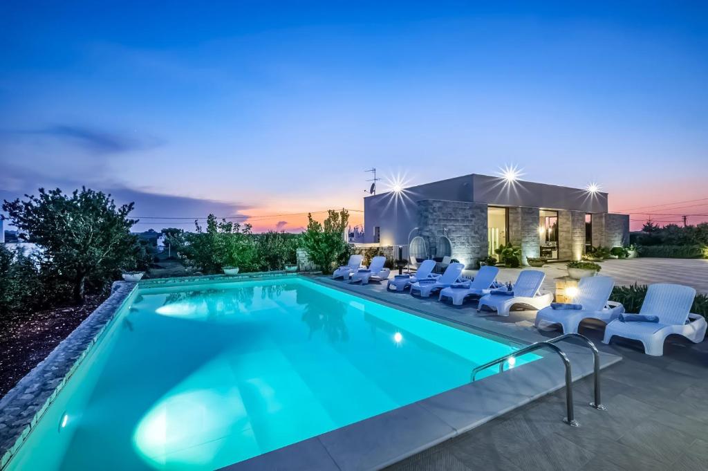 une piscine avec des chaises blanches et une maison dans l'établissement Villa Bella Ostuni by Villa Plus, à Ostuni