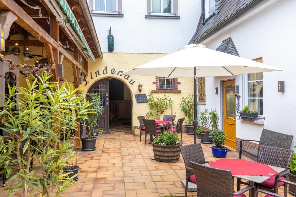 un patio extérieur avec des tables, des chaises et un parasol dans l'établissement Zur Lindenau, à Rüdesheim am Rhein