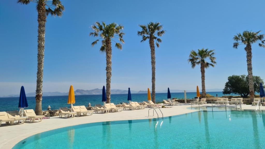 a swimming pool with palm trees and chairs and the ocean at Irina Beach Hotel in Tigaki