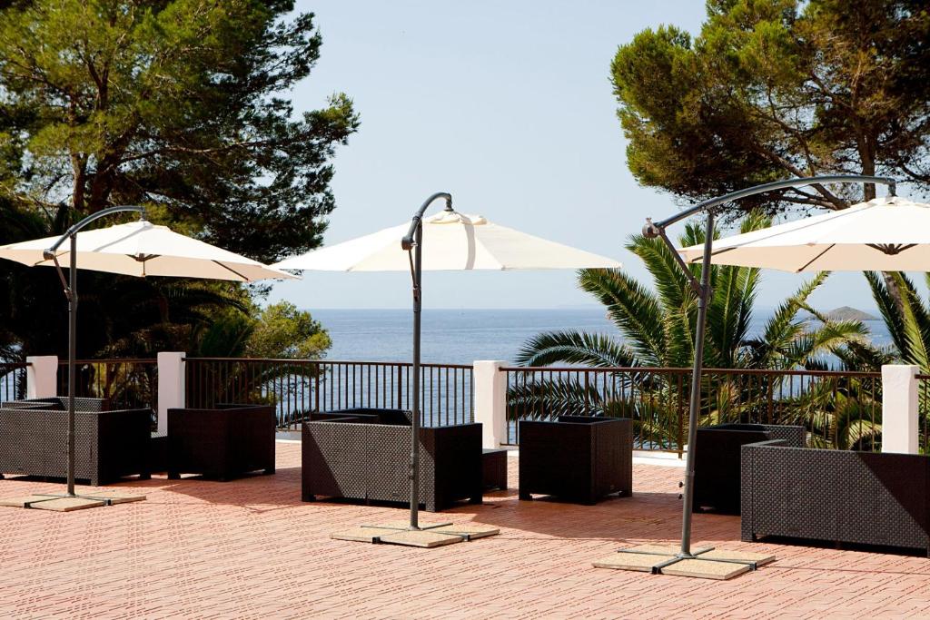 a patio with chairs and umbrellas and the ocean at Club Cala Azul in Cala Llenya