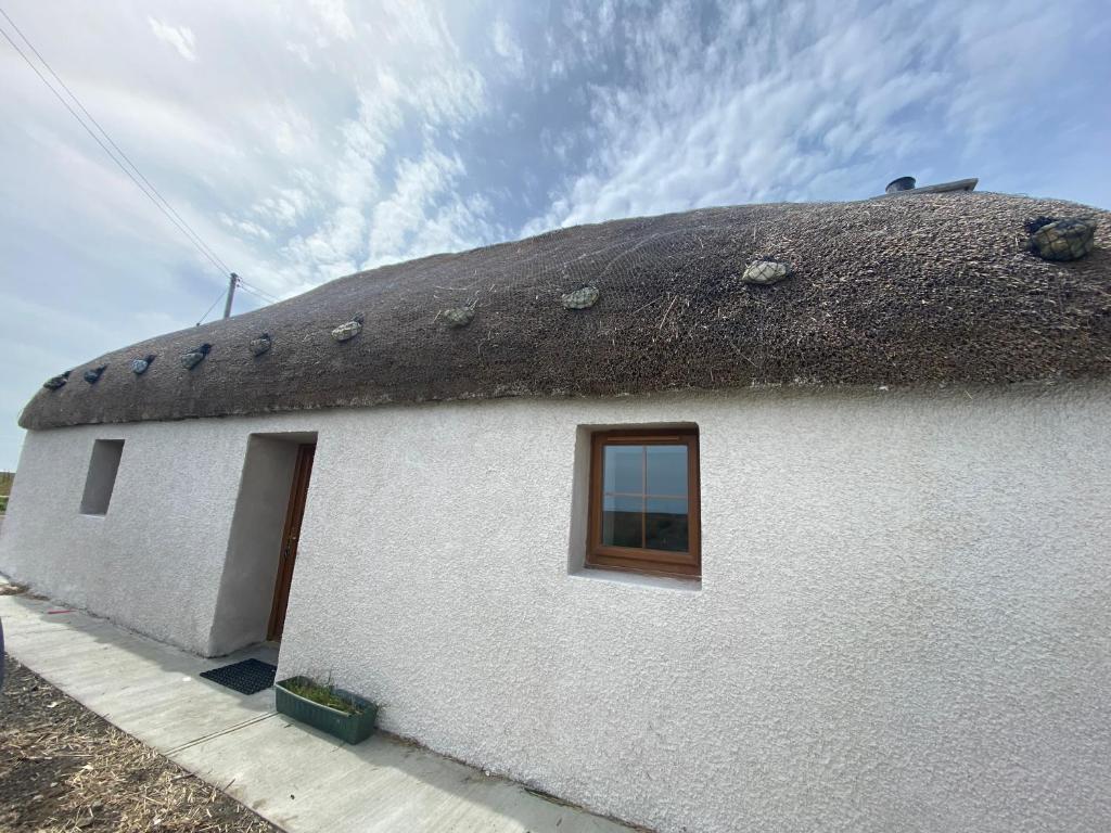 un edificio blanco con techo de paja y ventana en An Taigh Dubh- One bedroomed cottage, en Creagorry