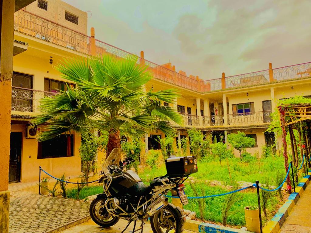 a motorcycle parked in front of a building with a palm tree at Hotel Restaurant La Kasbah in Tinerhir