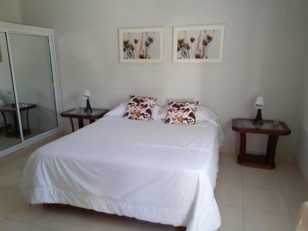 sypialnia z białym łóżkiem z poduszkami i dwoma stołami w obiekcie CASITA HOGAREÑA JARABACOA (independent entrance) w mieście Jarabacoa