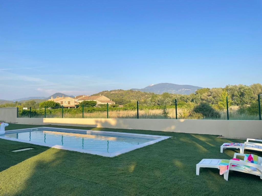 a swimming pool with two chairs on the grass at Villa au crestet à 5 minutes de Vaison la romaine in Crestet