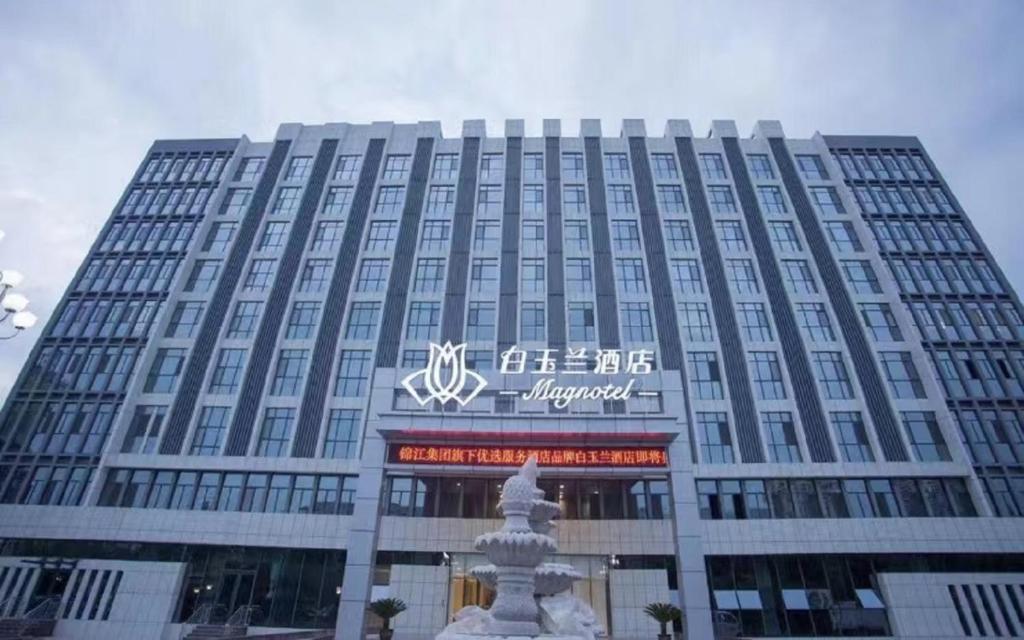 a large building with a sign in front of it at Magnotel Hotel of Jiaxiang Jining, Zengzi Ave hotel in Jining