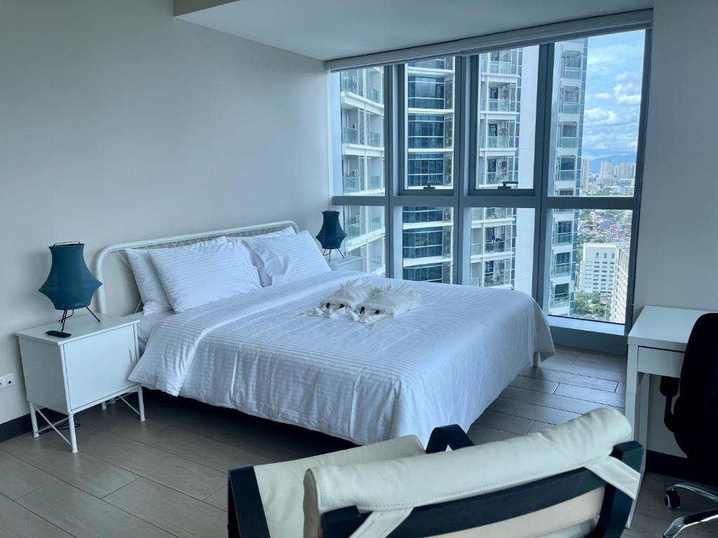 una camera con un letto bianco e una grande finestra di Bright 2-bedroom condo with pool in BGC Uptown a Manila