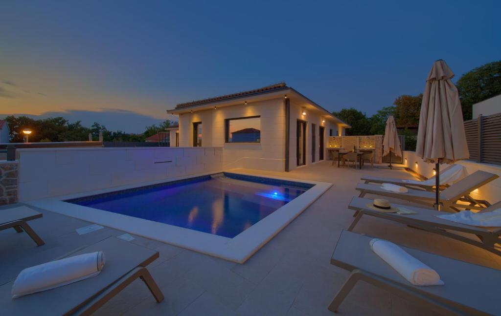 a swimming pool on a patio with chairs and an umbrella at Villa QUARNARO with heated pool in Omišalj