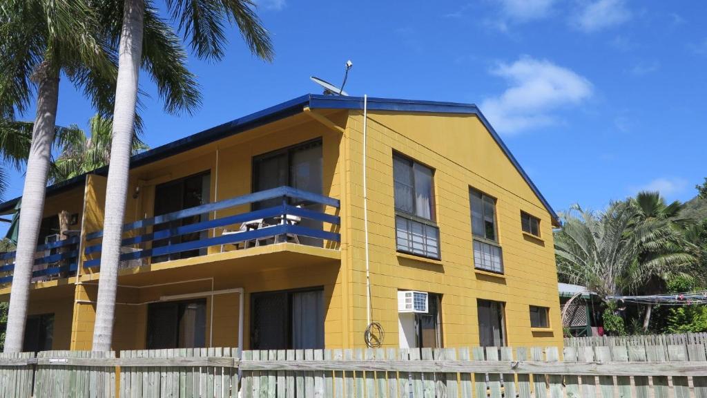 un bâtiment jaune avec des palmiers devant lui dans l'établissement Casual Lodge Unit 4, à Nelly Bay