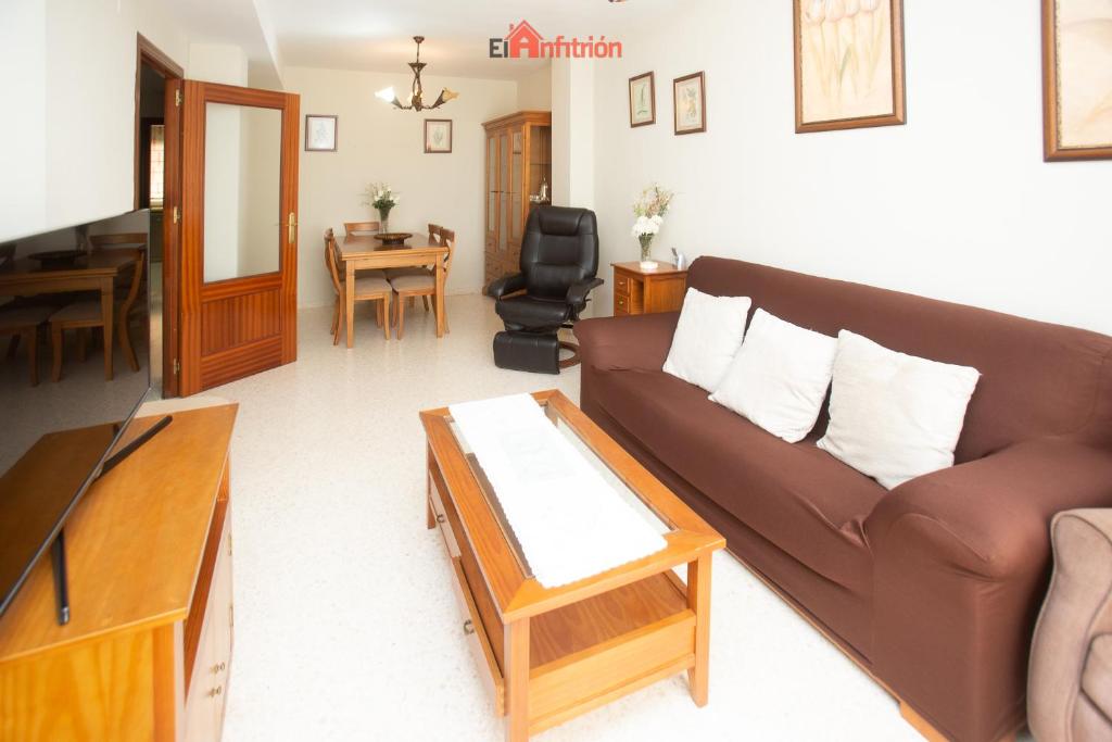 Una sala de estar con un sofá marrón y una mesa. en El Anfitrión - Dúplex Doña Ana, en Sanlúcar de Barrameda