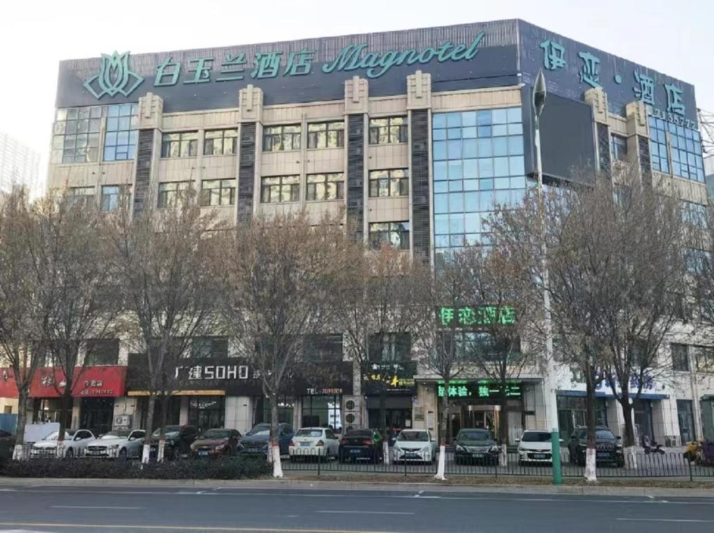 Magnotel Hotel Cangzhou International Hardware City في Cangzhou: مبنى كبير فيه سيارات تقف امامه