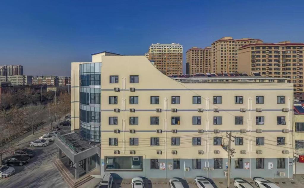 un gran edificio blanco con coches aparcados en un aparcamiento en Magnotel Binhai Bohai Five Road Hotel, en Binzhou