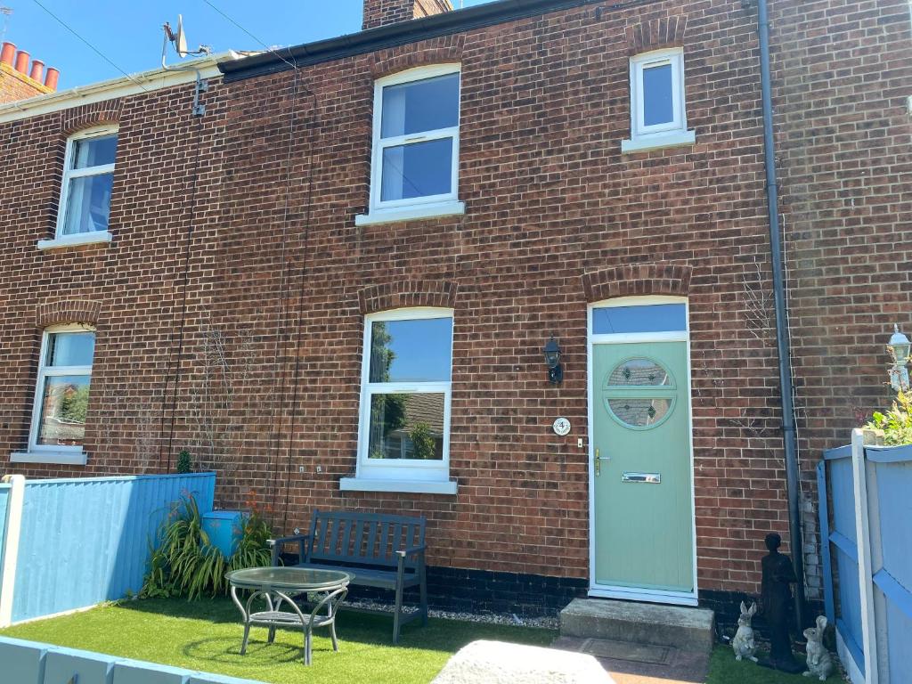 a brick house with a blue door and a table at Ivy Coastal Cottage in Caister-on-Sea