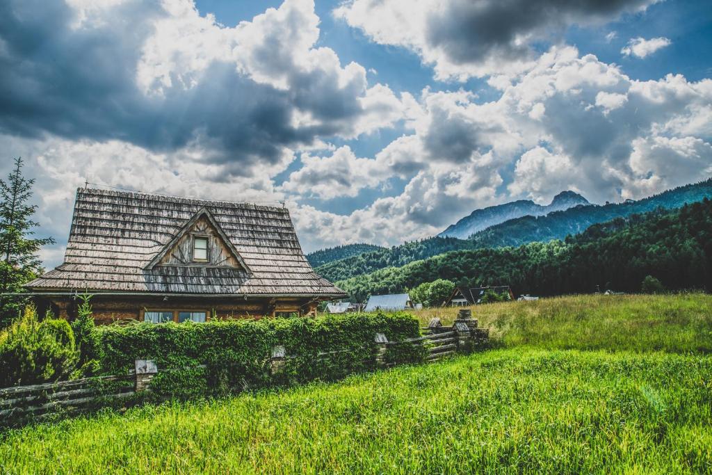 een oud huis in een veld met een hek en bergen bij TatryTop Domek pod Giewontem in Zakopane