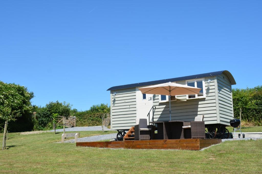 a tiny house with a patio and an umbrella at Kerswell Farm Shepherd Huts in Totnes