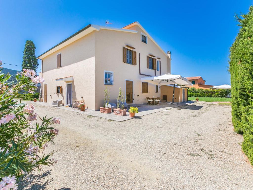 duży biały dom z parasolką na żwirowym podjeździe w obiekcie Apartment Benedetta by Interhome w mieście Castiglione della Pescaia