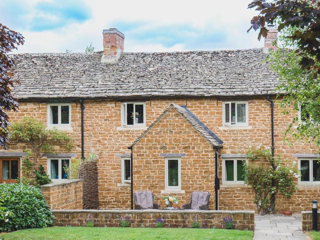 ein altes Backsteinhaus mit zwei Stühlen davor in der Unterkunft Climbing Rose Cottage - Dog Friendly - Peaceful Cotswold Cottage in Adlestrop