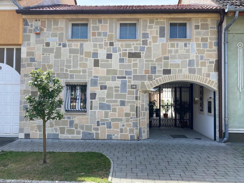 a stone house with a gate and a tree in front at KLAPKA PROVANCE APARTMAN in Kaposvár