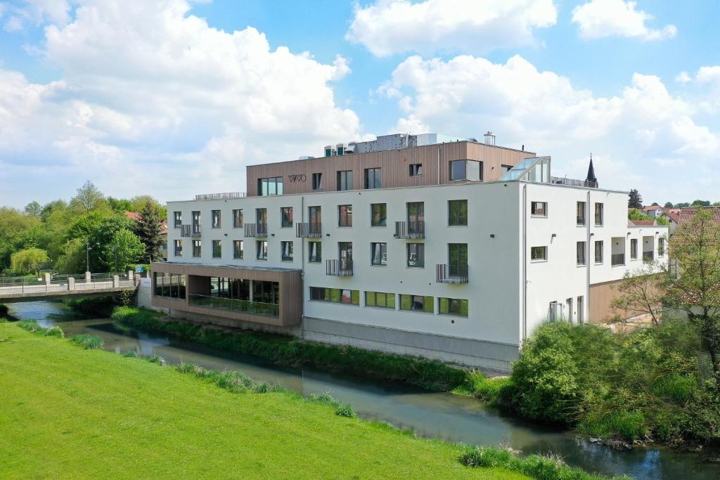 a white building next to a river with a bridge at Hotel VIVO in Schierling